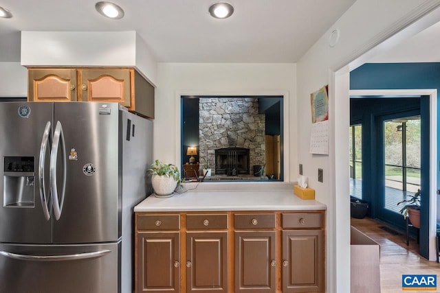 kitchen featuring stainless steel refrigerator with ice dispenser, light countertops, light wood-style flooring, and a stone fireplace