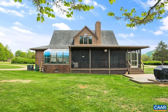 rear view of house with a lawn, a chimney, a sunroom, and central air condition unit