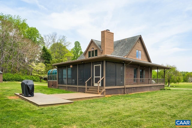 back of house with a lawn, a chimney, a sunroom, and brick siding