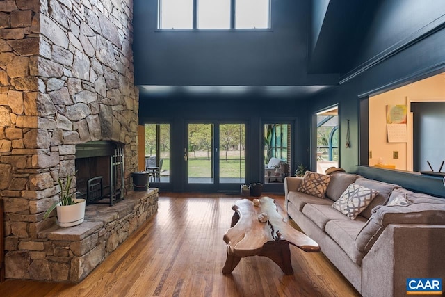 living room with a high ceiling, a stone fireplace, and wood finished floors