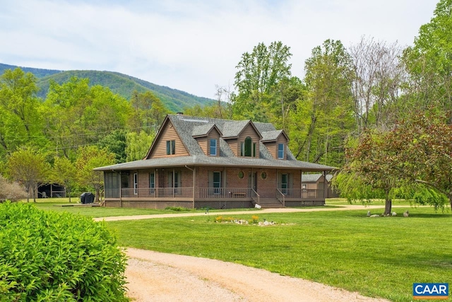 farmhouse-style home featuring brick siding, a front lawn, a mountain view, and covered porch