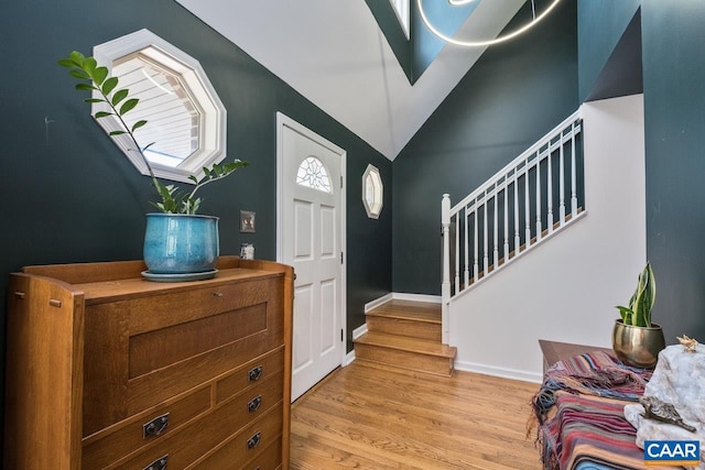 foyer with light wood-style floors, baseboards, vaulted ceiling, and stairway