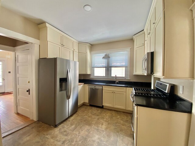 kitchen featuring dark countertops, cream cabinets, stainless steel appliances, and a sink