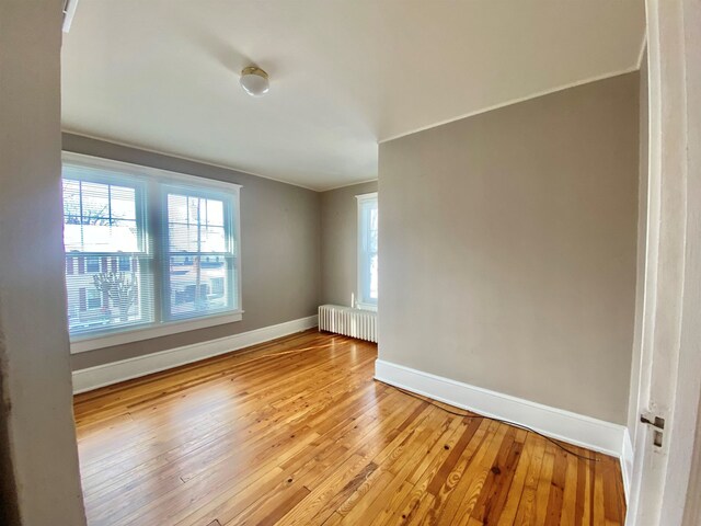 empty room with radiator, a healthy amount of sunlight, light wood-style flooring, and baseboards