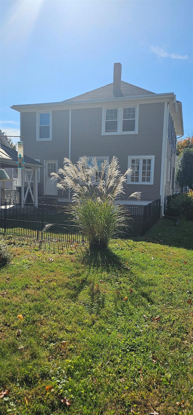 back of house featuring a chimney, fence, and a yard