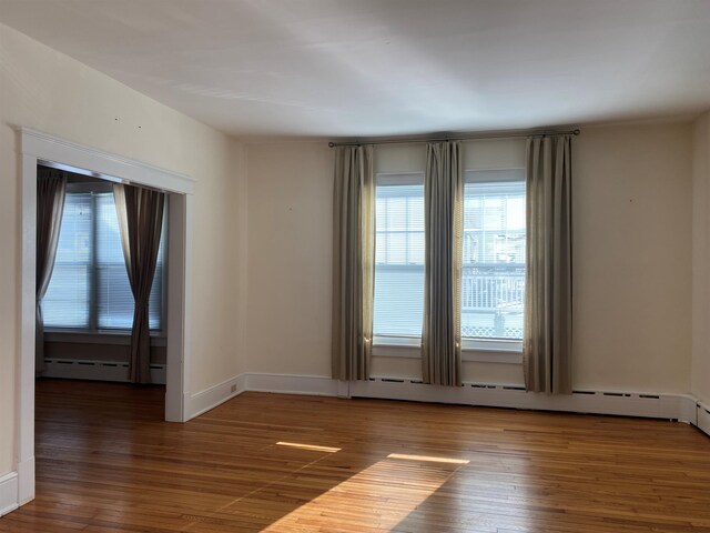 empty room featuring baseboards, a baseboard heating unit, and wood finished floors