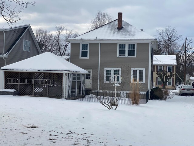 snow covered rear of property with a chimney