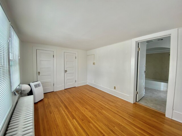 unfurnished bedroom with light wood finished floors, baseboards, and arched walkways