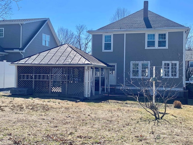 back of house with a sunroom, a shingled roof, and a chimney