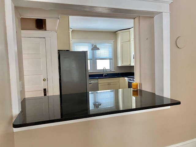 kitchen featuring stainless steel appliances, dark countertops, white cabinets, a sink, and a peninsula