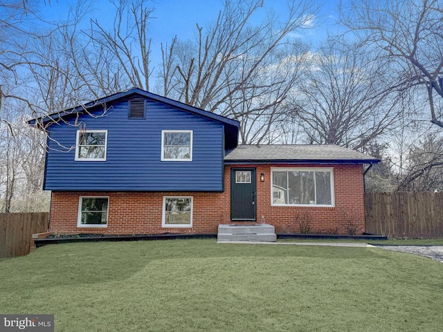 split level home featuring brick siding, a front yard, and fence