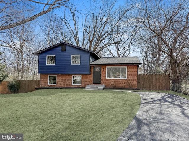 tri-level home featuring a front lawn, fence, brick siding, and aphalt driveway