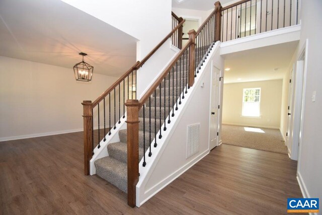 stairway with a towering ceiling, wood-type flooring, and a chandelier