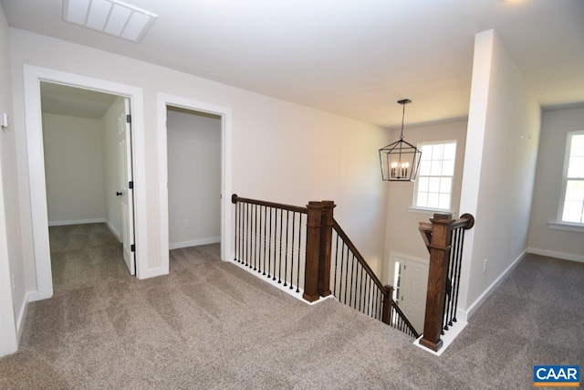 hallway featuring a notable chandelier, visible vents, carpet flooring, an upstairs landing, and baseboards