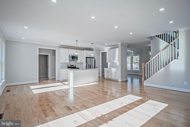 kitchen with appliances with stainless steel finishes, white cabinets, hanging light fixtures, a center island, and light hardwood / wood-style flooring