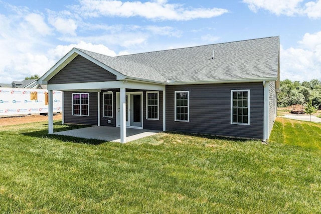 back of house with a yard, roof with shingles, and a patio area