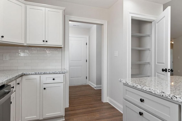 kitchen with dark wood-type flooring, white cabinetry, backsplash, stainless steel dishwasher, and baseboards