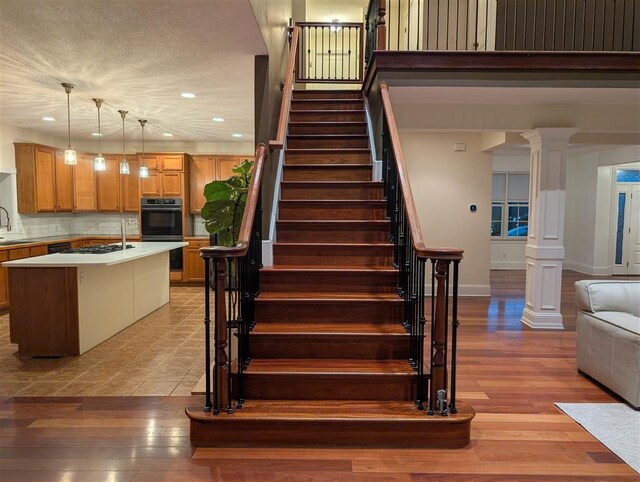 staircase with hardwood / wood-style flooring, sink, a textured ceiling, and ornate columns