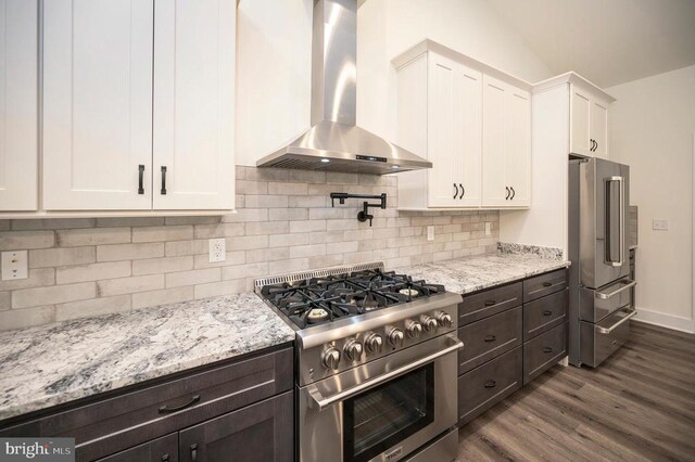 kitchen featuring white cabinets, high end appliances, light stone counters, dark wood-type flooring, and wall chimney range hood