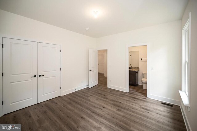 unfurnished bedroom with ensuite bath, dark hardwood / wood-style flooring, and a closet