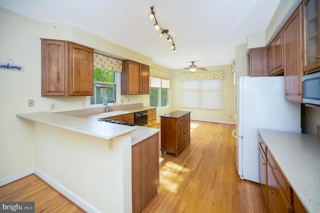 kitchen with black dishwasher, light wood-style floors, a sink, and brown cabinets