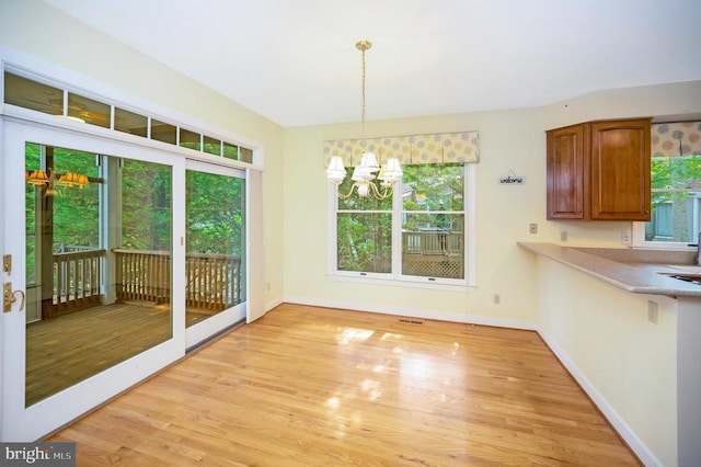 unfurnished dining area featuring light wood-style floors, baseboards, and a notable chandelier