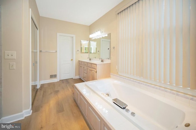 full bathroom featuring visible vents, vanity, wood finished floors, baseboards, and a bath