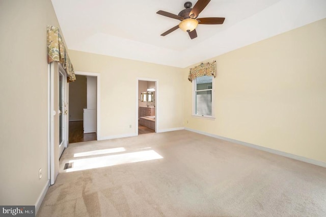 unfurnished bedroom featuring a tray ceiling, carpet flooring, ensuite bath, and baseboards