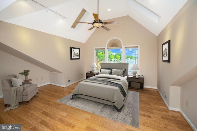 bedroom featuring baseboards, visible vents, wood finished floors, rail lighting, and high vaulted ceiling