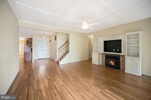 unfurnished living room featuring light wood-type flooring, coffered ceiling, stairway, and a tiled fireplace