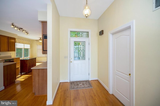 doorway featuring light wood finished floors, rail lighting, visible vents, a ceiling fan, and baseboards