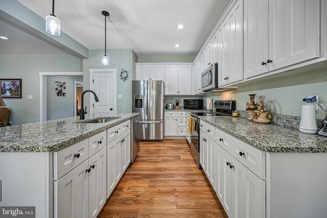 kitchen featuring light wood-style flooring, a sink, hanging light fixtures, white cabinets, and appliances with stainless steel finishes