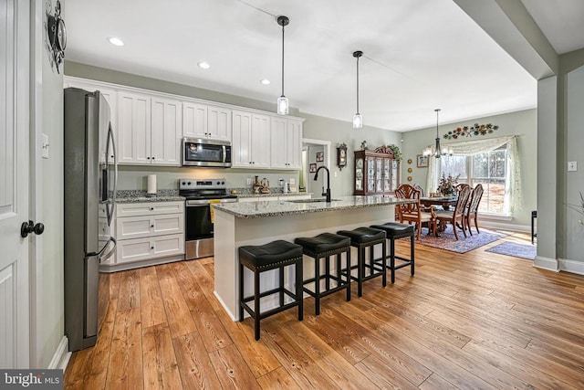 kitchen featuring light stone countertops, light wood-type flooring, appliances with stainless steel finishes, white cabinetry, and a sink