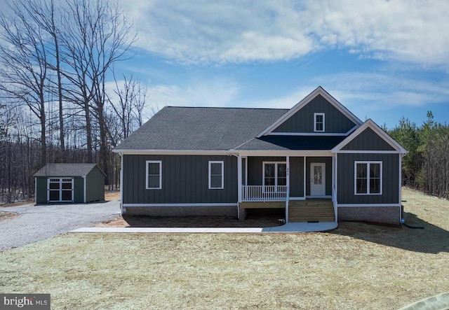 view of front facade featuring a shed, board and batten siding, covered porch, an outdoor structure, and roof with shingles