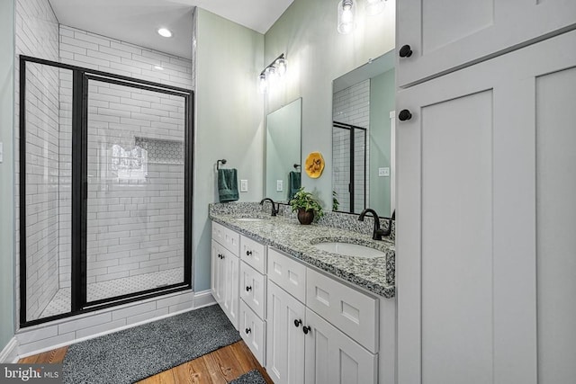 bathroom featuring double vanity, wood finished floors, a stall shower, and a sink