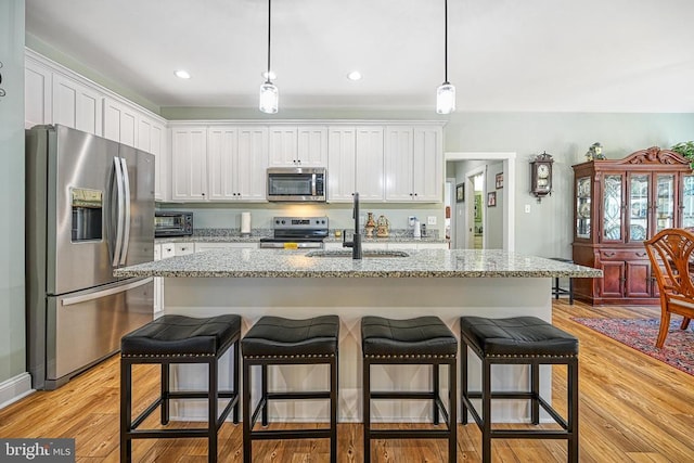 kitchen with light wood finished floors, pendant lighting, appliances with stainless steel finishes, white cabinetry, and a sink