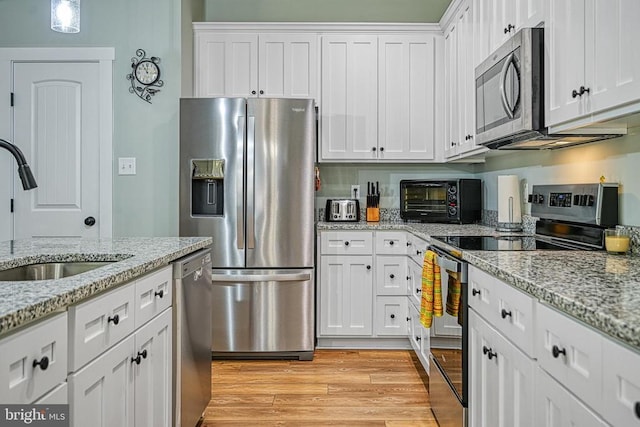 kitchen featuring a toaster, appliances with stainless steel finishes, light wood-style floors, white cabinets, and a sink