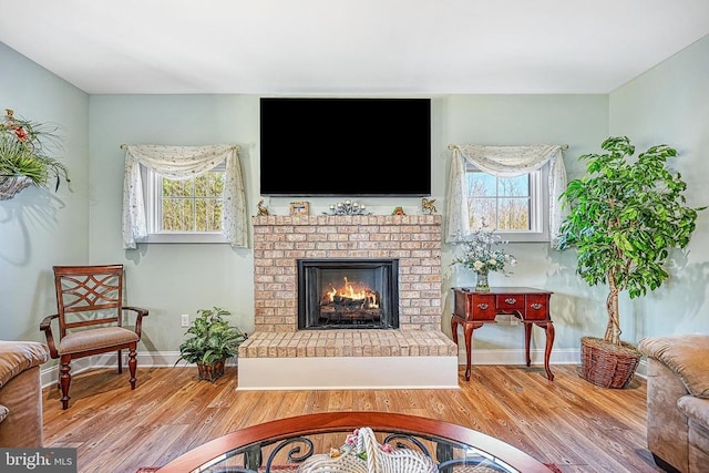 living area with baseboards, a brick fireplace, and wood finished floors