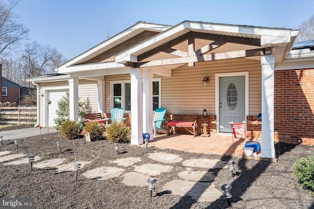 exterior space with a porch, brick siding, fence, and an attached garage