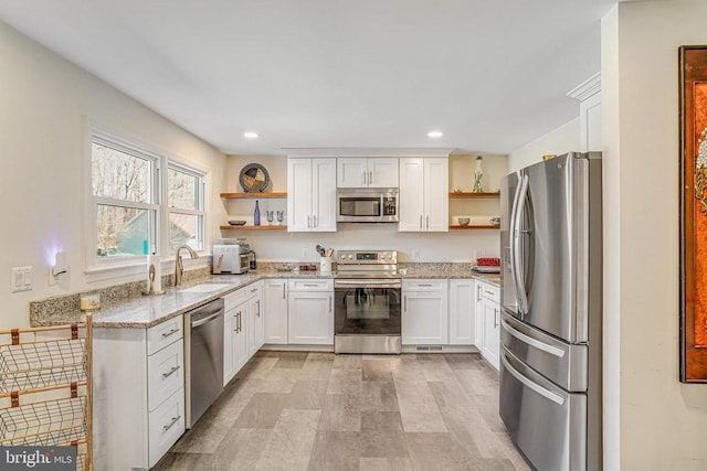 kitchen with stainless steel appliances, white cabinetry, a sink, and open shelves