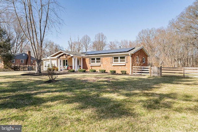 view of front of house featuring solar panels, brick siding, a front lawn, and fence