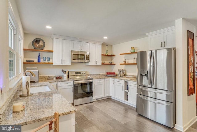 kitchen with stainless steel appliances, a sink, white cabinetry, light stone countertops, and open shelves