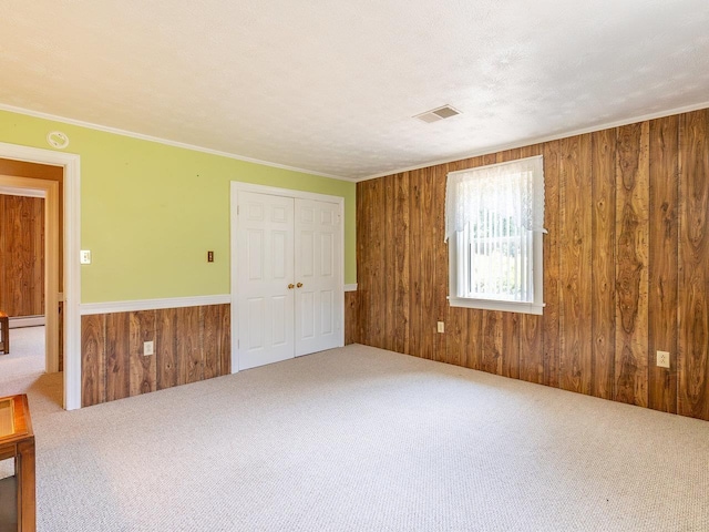 empty room featuring ornamental molding, a textured ceiling, carpet, and wood walls