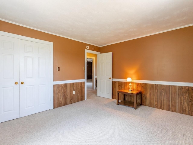 unfurnished bedroom with ornamental molding, wooden walls, light colored carpet, and a closet