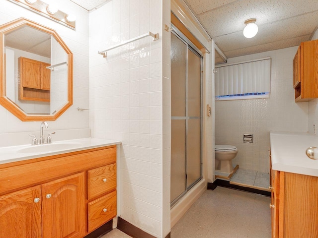 bathroom featuring a paneled ceiling, tile walls, vanity, toilet, and walk in shower