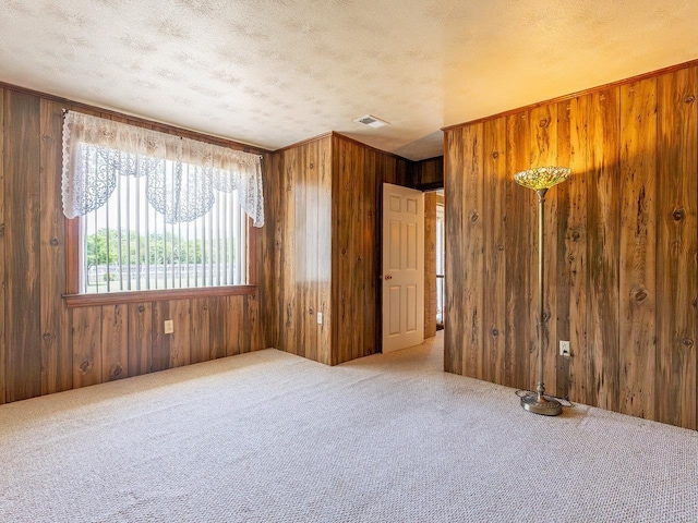 carpeted spare room with a textured ceiling and wood walls