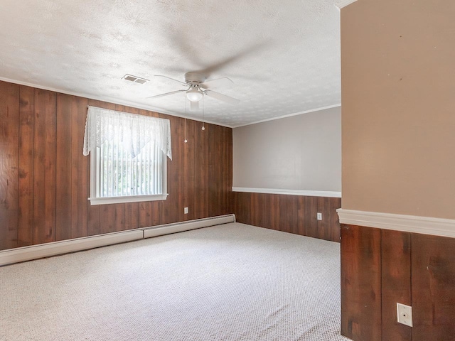 carpeted empty room with wood walls, a baseboard heating unit, ceiling fan, crown molding, and a textured ceiling