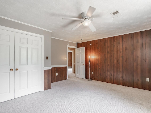 unfurnished bedroom with wooden walls, ornamental molding, a textured ceiling, light colored carpet, and a closet