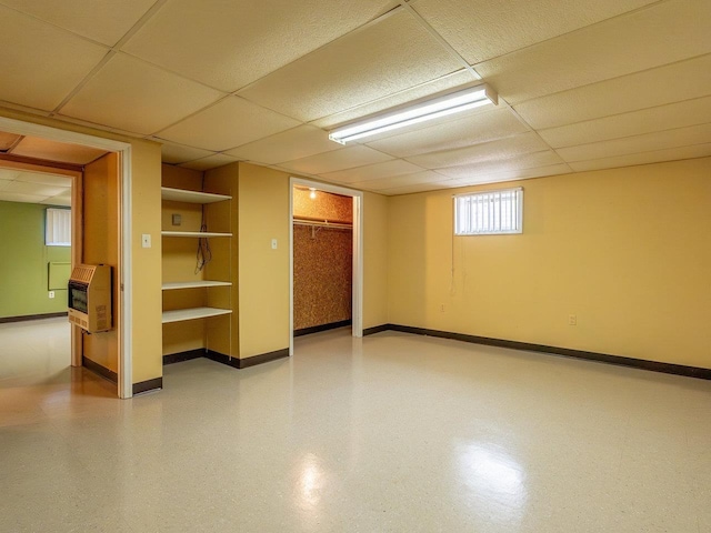 basement with a paneled ceiling and heating unit