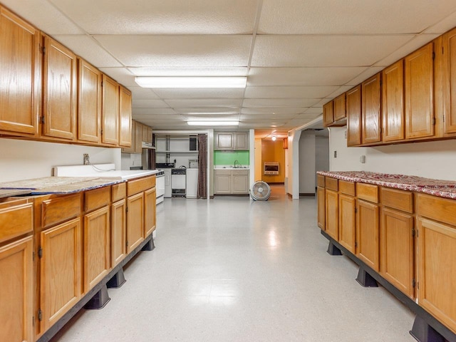 kitchen with light stone counters, sink, heating unit, and a drop ceiling